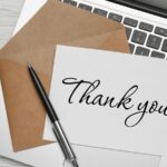 A client appreciation thank-you card on a laptop keyboard with a pen and an open brown envelope.