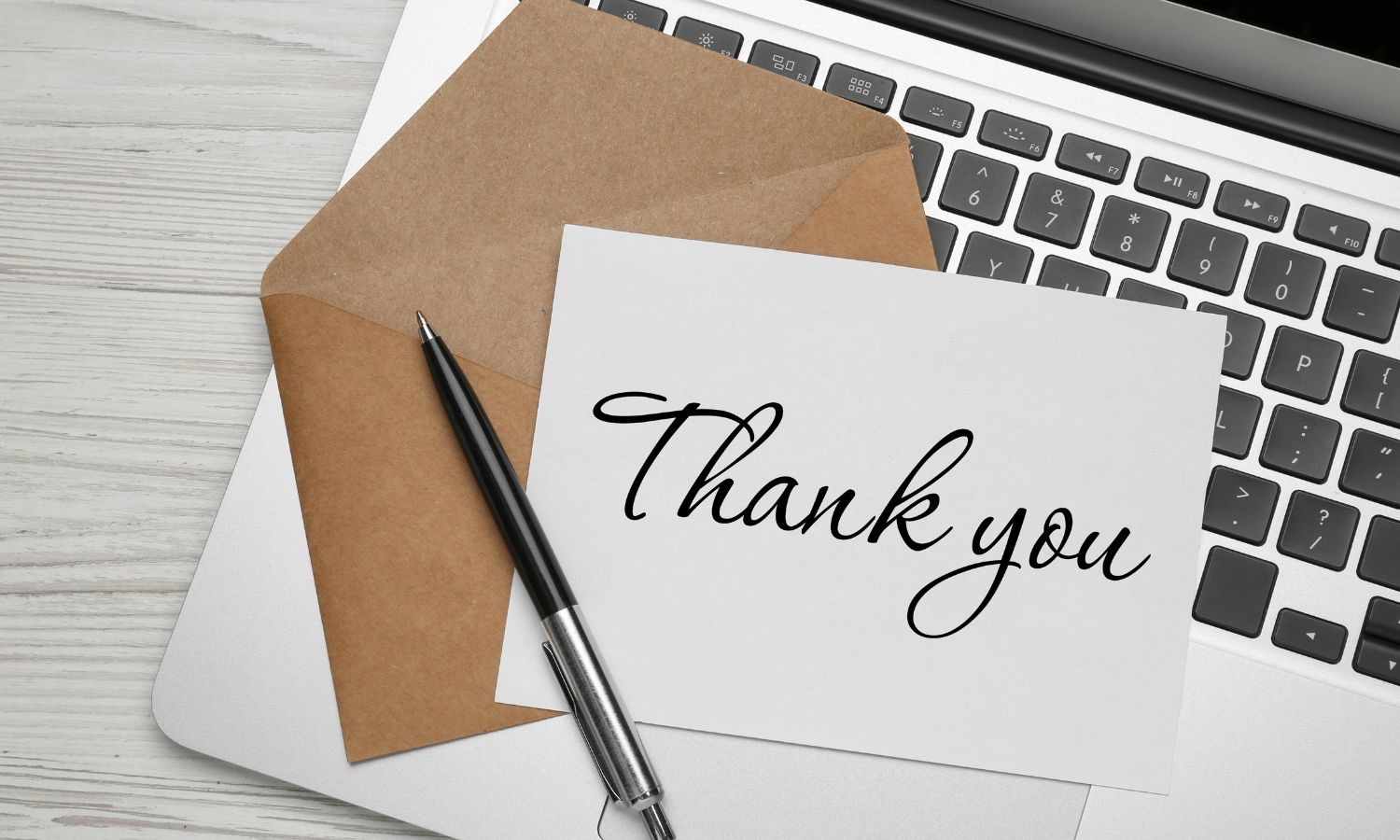 A client appreciation thank-you card on a laptop keyboard with a pen and an open brown envelope.
