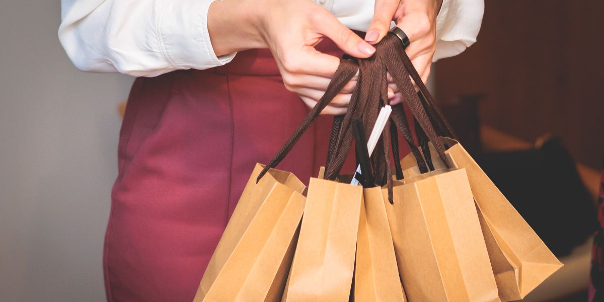 Close-up of a person holding several brown gift bags by their handles.