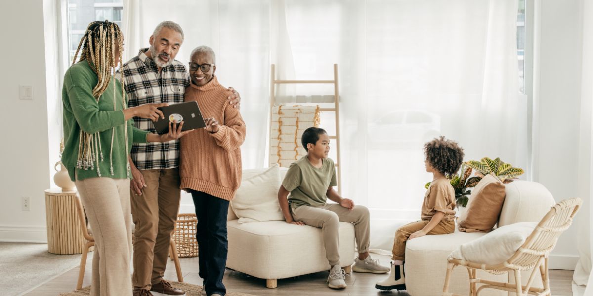 A family of four smiling and gathered together, with two adults standing and two children sitting in a cozy, well-lit living room