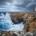 Sturdy lighthouse stands firm against crashing waves during a storm, its powerful light cutting through the dark sky to gu...