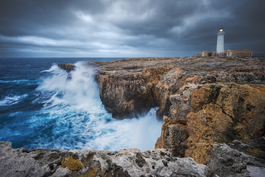 Sturdy lighthouse stands firm against crashing waves during a storm, its powerful light cutting through the dark sky to gu...