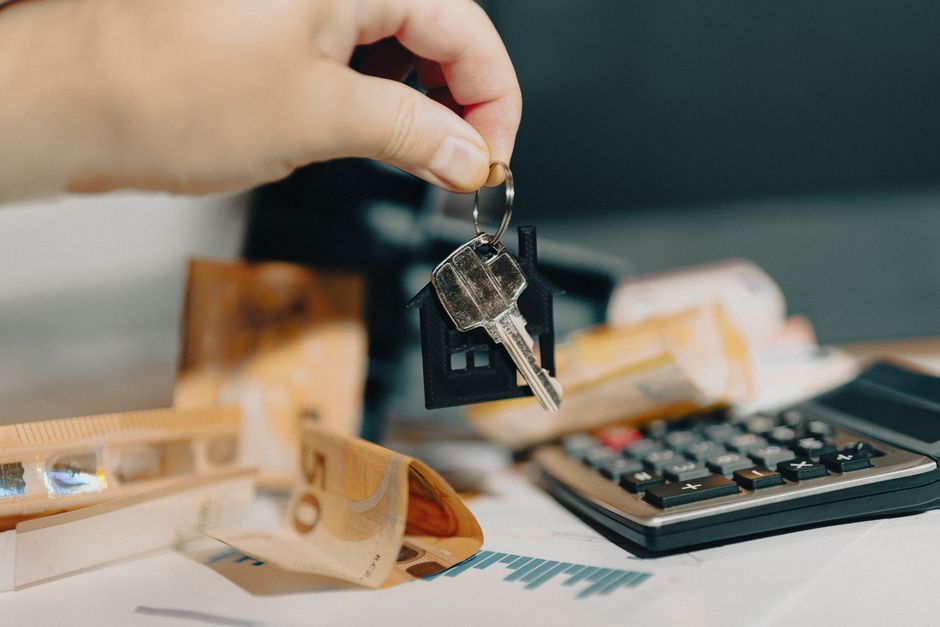 A clean, overhead view of a minimalist desk with a calculator, a pen, and a set of house keys, illustrating the financial calculations involved in selling a home.