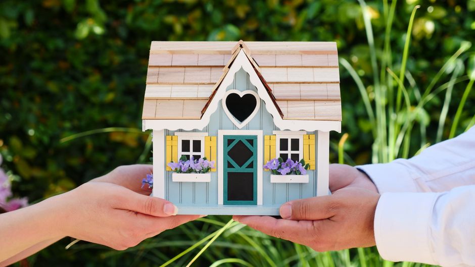 A close-up of a person's hands carefully holding a small model of a house, representing real estate as a tangible asset and financial investment.