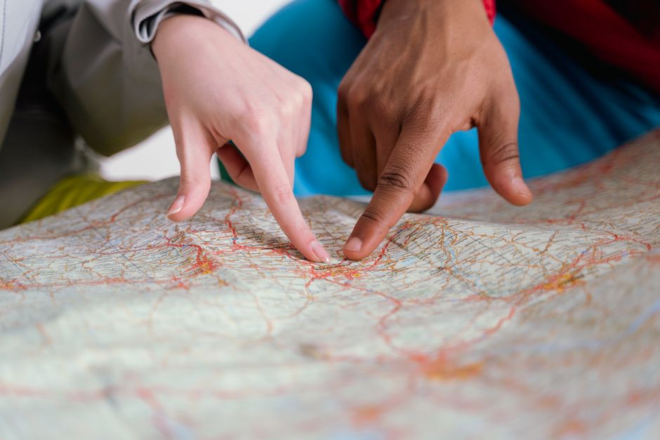 A minimal, top-down view of hands pointing to a specific location on a map spread across a modern desk, representing the precision of a strategic GEO-targeting SEO service.